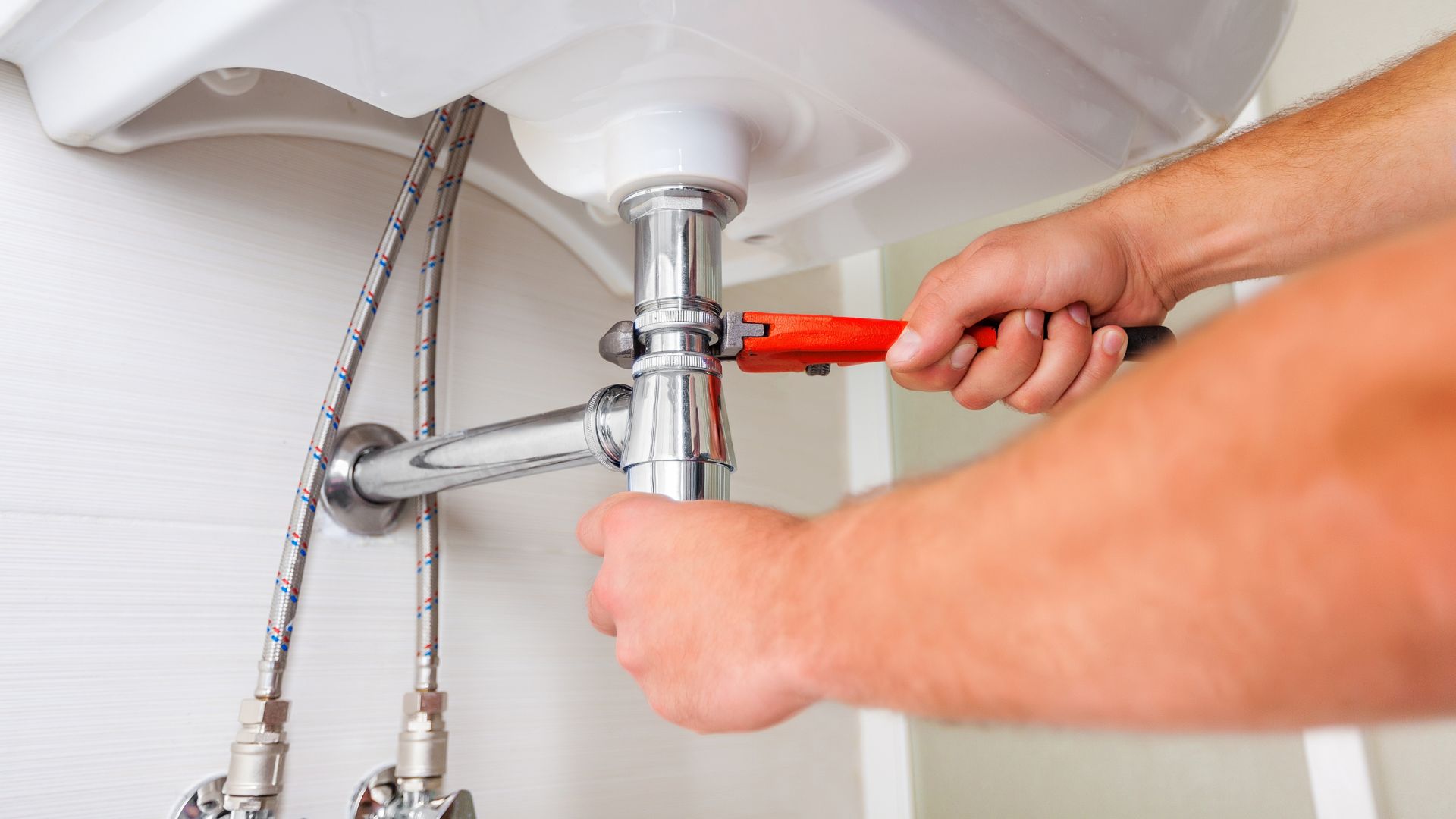 A man fixing a bathroom sink with a wrench